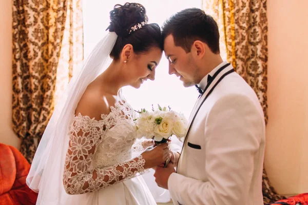 Os recém-casados felizes estão segurando o buquê de casamento enquanto estão frente a frente . — Fotografia de Stock