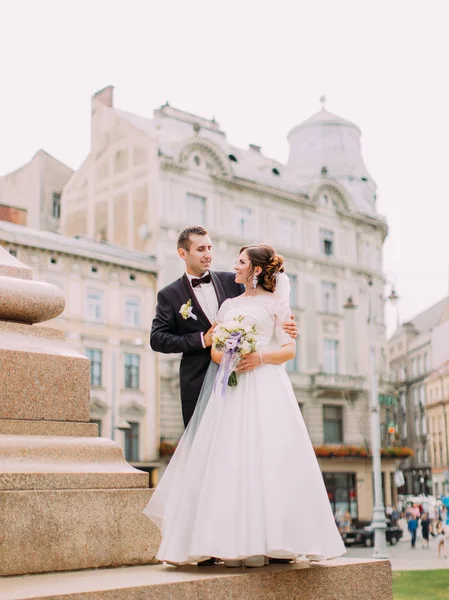 Ganzkörperaufnahme des Bräutigams, der die Braut im Hintergrund der Innenstadt umarmt. — Stockfoto