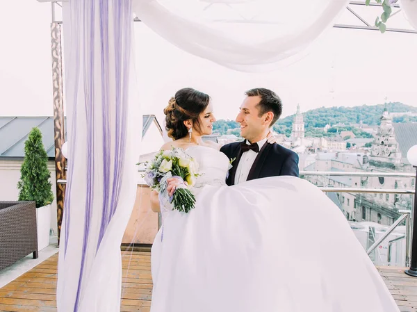 Phoro horizontal dos recém-casados felizes. O noivo leva a noiva perto do arco . — Fotografia de Stock