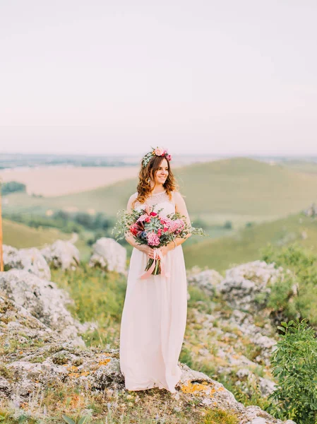 Bella sposa con l'enorme bouquet da sposa sta guardando da parte mentre in piedi sulle rocce . — Foto Stock