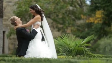 Yeni evliler yavaşça öpüşmek çok güzel çift romantik duygusal portre. Yakışıklı damat onun büyüleyici gelin kaldırma. Bahçe yeri.