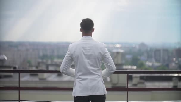 Achteraanzicht van de onbekende stijlvolle man in een wit pak permanent op het terras en genieten van het landschap. — Stockvideo