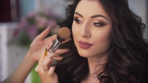 La hermosa actriz se está preparando para el rodaje. Artista de maquillaje desconocido está aplicando maquillaje en la cara de la mujer con el pelo largo y rizado . — Vídeos de Stock