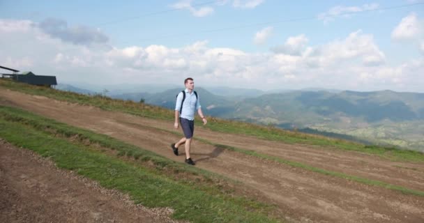 Osamělé procházce v horách. Pohledný mladý muž chodí po kopci s batohem na svých bedrech a rozhlíží se na oblohu — Stock video