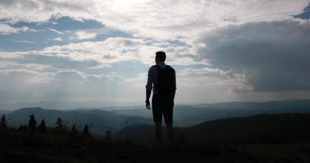 Lonely walk in the mountains. Look from behind at a man with backpack standing before beautiful mountain landscape and cloudy sky over it — Stock Video