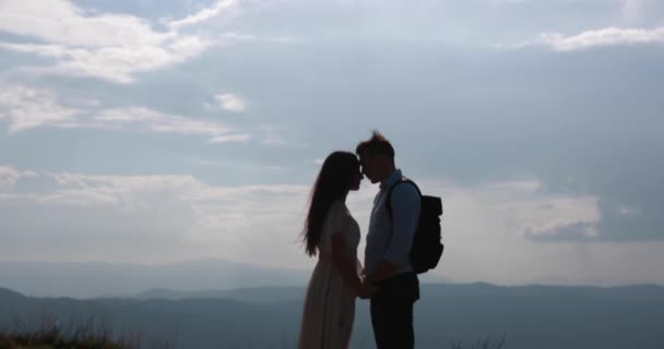 Ensamheten i bergen. Man och kvinna håll varandra händer anbud och kiss stående på toppen av en kulle med vackra landskapet bakom dem. — Stockvideo