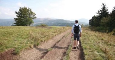 Yalnız yürüme dağlarda. Adam yolda bir tepe ile ondan önce büyük peyzaj üzerinde yürür ve omzunun üzerinden görünüyor