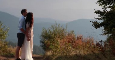 Dağlarda seviyorum. Adam hugs kadın arkadan ihale ve onu izlerken günbatımı bir tepe üzerinde dağların üzerinden öpücük