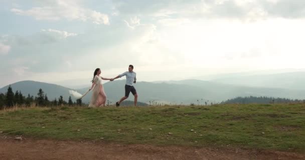 Amor en las montañas. El hombre y Woiman corren a lo largo del camino hacia el horizonte en algún lugar de la colina mientras el sol brilla sobre ellos — Vídeo de stock