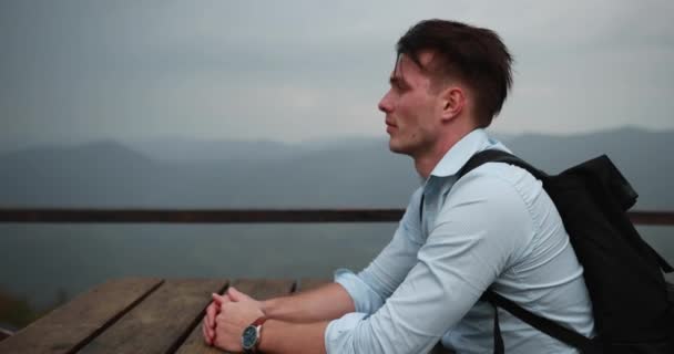 Eenzame man in de bergen. Jonge knappe man ligt zijn hoofd op de armen zitten aan de tafel met prachtig uitzicht rondom hem en regen hem omvallen — Stockvideo
