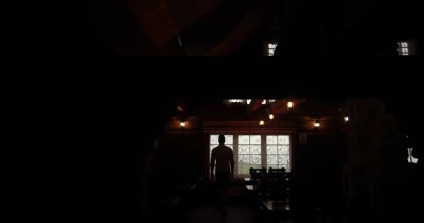 Solidão. Homem caminha em direção a uma janela em uma casa escura observando como a chuva cai fora — Vídeo de Stock