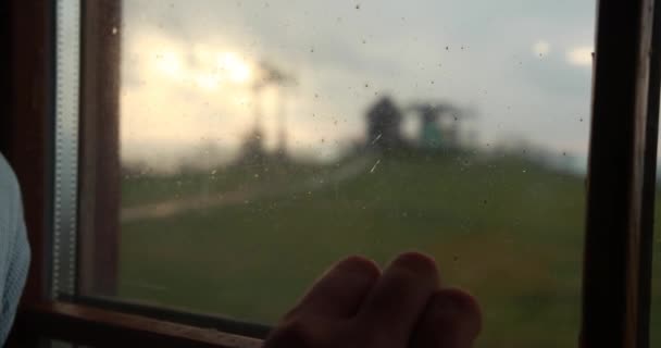Человек кладет руку на окно с индустриальным горным ландшафтом позади него и красочным вечерним небом — стоковое видео