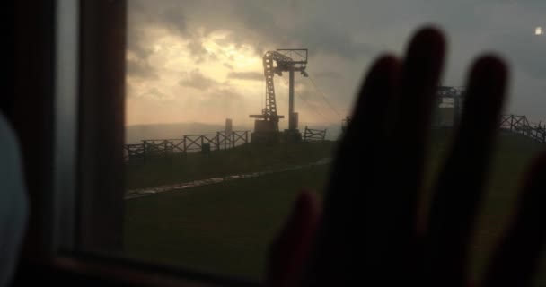 Man puts his arm on the window with industrial mountain landscape behind it and colorful evening skies — Stock Video