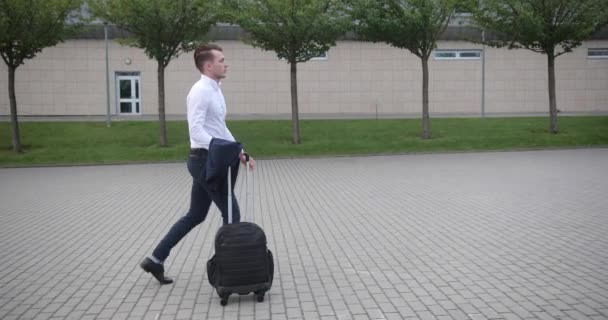 Empresario en el trabajo. Joven guapo con camisa blanca camina desde un aeropuerto con una maleta — Vídeo de stock
