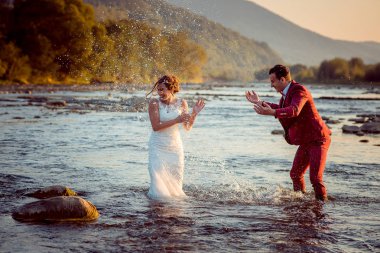 Mutlu yeni evli çift günbatımı sırasında nehirde su ile oynuyor. Damat gelini su sıçramasına.