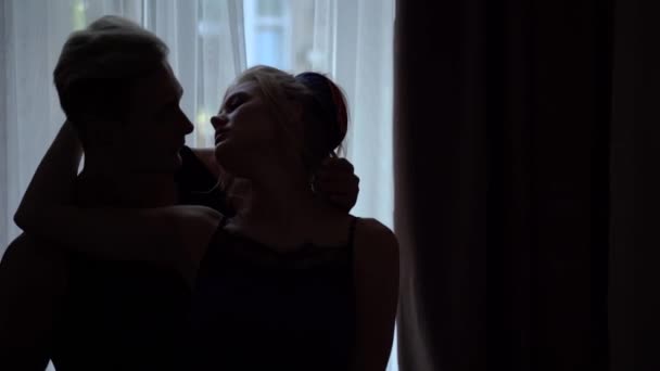 Силуэты молодых мужчин и женщин, прикасающихся друг к другу нежно перед ярким окном в комнате — стоковое видео