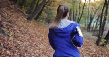 Kadın atlet parkında. Mavi ceketli güzel kadın ve diğer fitness giyim dinler müzik o parkta sunshine tam düşen yapraklar üzerinde çalışırken