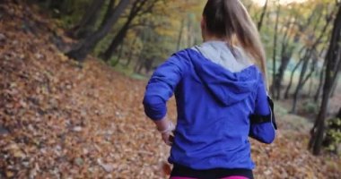 Kadın atlet parkında. Mavi ceketli güzel kadın ve diğer fitness giyim dinler müzik o parkta sunshine tam düşen yapraklar üzerinde çalışırken