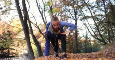 Parkta çalışma dışarı. Mavi ceketli genç kadın onun kolları ve bacakları güzel sonbahar park germe çalıştırmak için hazır hale getirilir