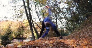 Parkta çalışma dışarı. Mavi ceketli genç kadın onun kolları ve bacakları güzel sonbahar park germe çalıştırmak için hazır hale getirilir