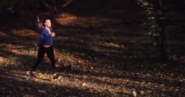 Kadın atlet parkında. Mavi ceketli güzel kadın ve diğer fitness giyim dinler müzik o parkta sunshine tam düşen yapraklar üzerinde çalışırken