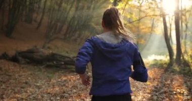 Kadın atlet parkında. Mavi ceketli güzel kadın ve diğer fitness giyim dinler müzik o parkta sunshine tam düşen yapraklar üzerinde çalışırken