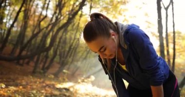 Kadın atlet parkında. Yorgun genç kadın bir süre güneş uzun riun sonra parlar arkasında altın ağaçlar üzerinde mola fitness elbiseli Close-up