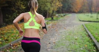 Kadın atlet parkında. Renkli Koşu elbiseli kadın müziği dinliyor ve parkta yol boyunca çalışır