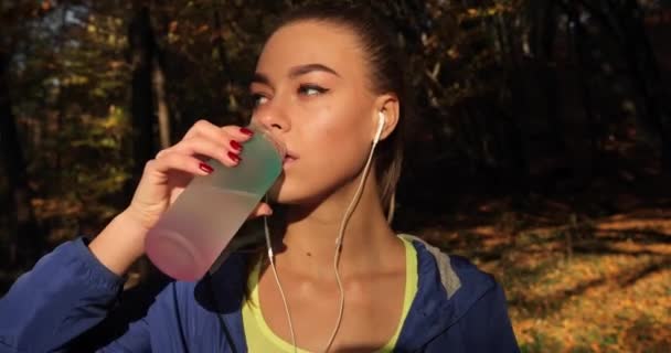 Läuferin im Park. Frau trinkt Wasser im herbstlichen Park, der mit herabgefallenem Laub bedeckt ist — Stockvideo