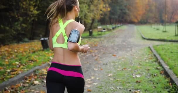 Kobiece runner w parku. Kobieta w stroju do biegania kolorowe słucha muzyki i biegnie wzdłuż ścieżki w parku — Wideo stockowe