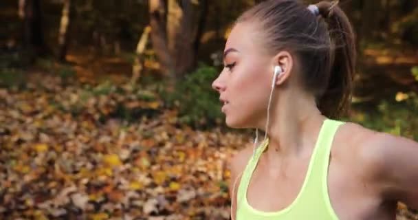 Corredor femenina en el parque. Mujer en traje de jogging colorido escucha la música y corre a lo largo del camino en el parque — Vídeo de stock