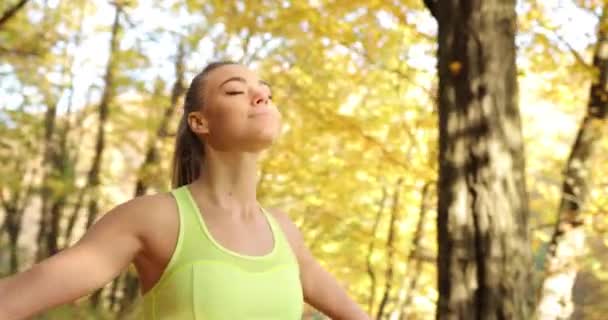 Vrouwelijke atleet in het park. Vrouw in pak joggen opgezocht in de lucht terwijl u ontspant nadat uitgevoerd in een herfst park — Stockvideo