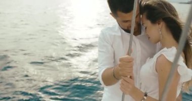 İki yat rahatlatıcı aşık. Adam hugs onu ihale ayakta beyaz yatta iken bayanlar elbise rüzgar esiyor