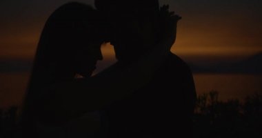 Sunset'teki aşk hikayesi. Onlar akşam ışık ışınları kıyısında stand iken Sillhouetes erkek ve kadın birbirlerini öpmeye ihale