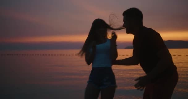 História de amor ao pôr-do-sol. Homem e mulher se divertem andando ao longo da costa do lago — Vídeo de Stock