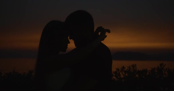 Historia miłości na zachód słońca. Sillhouetes mężczyzny i kobiety całujących się składania ofert, podczas gdy stoją na brzegu w promienie światła wieczorem — Wideo stockowe