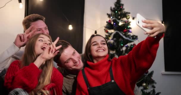 Celebración de Año Nuevo. Dos parejas jóvenes toman una selfie en el teléfono inteligente sentado delante de un árbol de Navidad — Vídeos de Stock