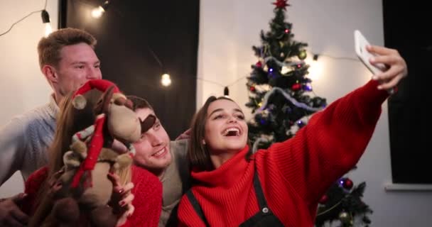 Νέο έτος γιορτή. Δύο νεαρά ζευγάρια κτήτορας μια selfie στο smartphone συνεδρίασης πριν από ένα χριστουγεννιάτικο δέντρο — Αρχείο Βίντεο