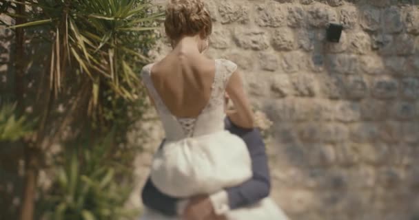 Matrimonio in Montenegro. Cerimonia tradizionale europea. Mattina prima del ricevimento. 4k. Sposo vortici bella sposa bionda sulle braccia in piedi al di fuori — Video Stock