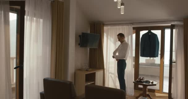 Wesele w Czarnogóra. Tradycyjne Europejskiej ceremonii. Rano przed recepcją. 4 k. szczęśliwy pary młodej wygląda rozwiązuje jego spinki do mankietów przed okna w pokoju hotelowym — Wideo stockowe