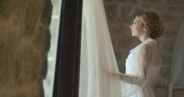 Γάμος στο Μαυροβούνιο. Παραδοσιακή ευρωπαϊκή τελετή. Το πρωί πριν από την υποδοχή. 4 k. νύφη στο λεπτό μετάξι ρόμπα φαίνεται μέσα από το παράθυρο, προετοιμασία για την γιορτινή ημέρα — Αρχείο Βίντεο