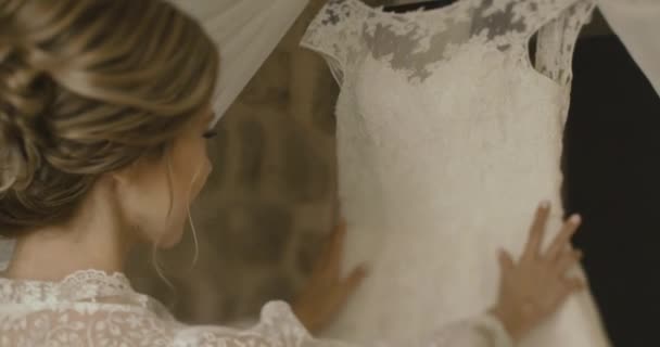 Γάμος στο Μαυροβούνιο. Παραδοσιακή ευρωπαϊκή τελετή. Το πρωί πριν από την υποδοχή. 4 k. νύφη στο λεπτό μετάξι ρόμπα θαυμάζει her γαμήλιο φόρεμα που στέκεται σε ένα δωμάτιο ξενοδοχείου — Αρχείο Βίντεο