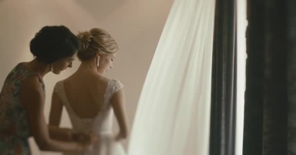 Γάμος στο Μαυροβούνιο. Παραδοσιακή ευρωπαϊκή τελετή. Το πρωί πριν από την υποδοχή. 4 k. μητέρα βοηθά όμορφο ξανθιά νύφη να βάλει σε ένα γαμήλιο φόρεμα — Αρχείο Βίντεο