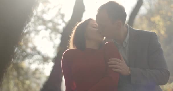 4k. 秋天的气氛。男人从后面抱着温柔的女人, 用金色的叶子亲吻站在秋天公园的她 — 图库视频影像