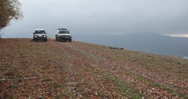 Turistické aktivity, exreme. 4 k. zpomaleně. Dvě extrémní terénní auta Nissan Patrol a Mitsubishi Pajero jízdy na horské silnici pokryté spadaného listí. Mlha nad kopce. — Stock video