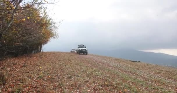 Actividades turísticas, exreme. 4k. Dos coches todoterreno extremos Nissan Patrol y Mitsubishi Pajero que conducen rápido por la carretera de montaña cubierta de hojas caídas. Niebla sobre las colinas . — Vídeos de Stock