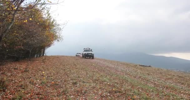 Touristic activities, exreme. 4k. Slow motion. Two extreme off-road cars Nissan Patrol and Mitsubishi Pajero driving fast on mountain road covered with fallen leaves. Fog over the hills. — Stock Video