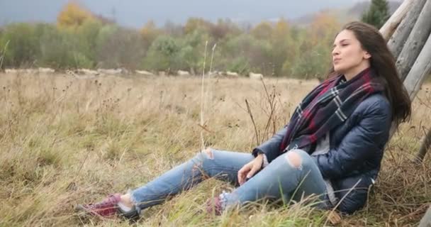 Mountain leisure. Autumn vocations. Attractive brunette woman in jeans ans leather jacket sits on the hill and looks thoughtful at mountains covered with fog — Stock Video