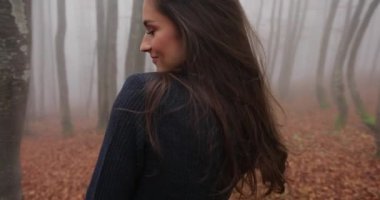 Sonbahar vibes, sisli orman. Uzun saçlı çekici esmer kadın rahat kıyafet giyer ve düşen yapraklar ile kaplı orman genelinde yürür. Olumlu duygular, mutluluk, döne döne
