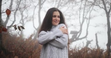 Sonbahar vibes, rahat bir atmosfer. Uzun siyah saçlı esmer kadın büyüleyici kendini ayakta sis ile kaplı sonbahar ormandaki kucaklayan